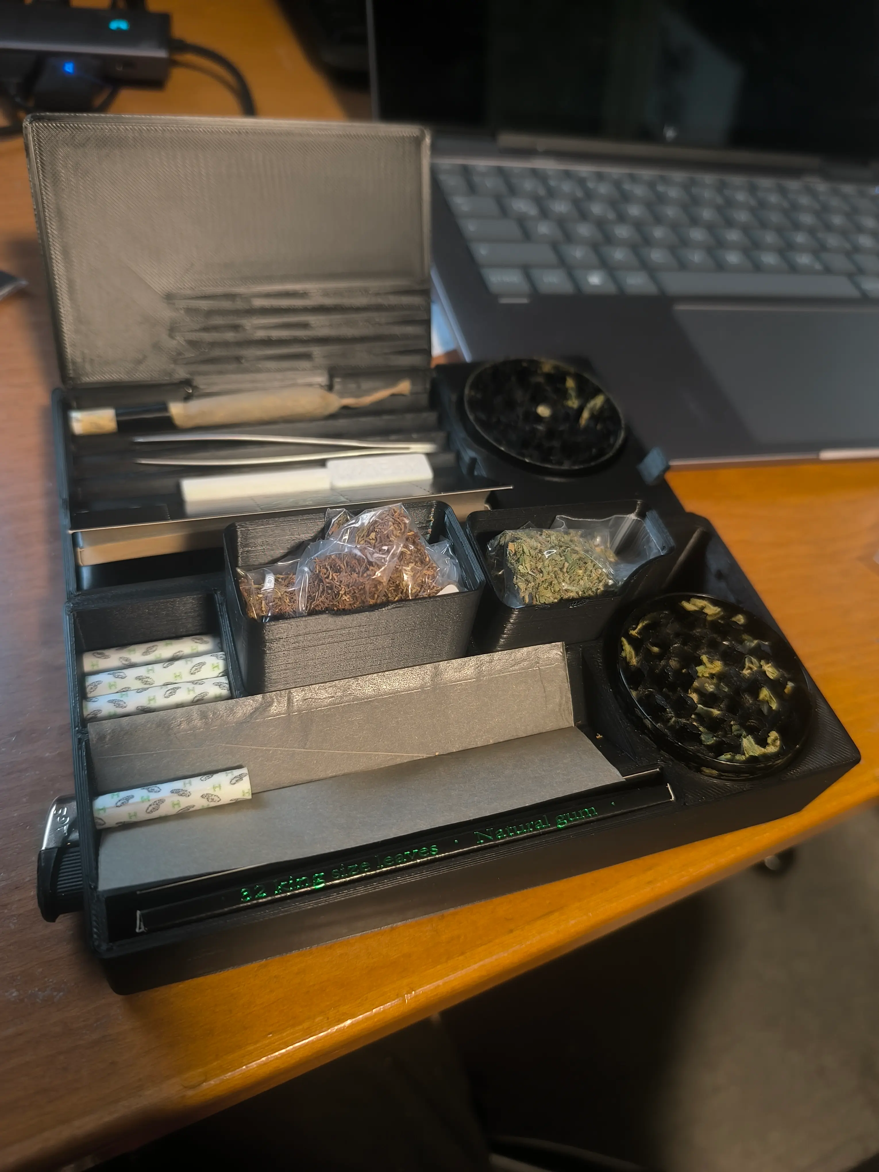 420-Box V11 Joint-Organizer aus schwarzem 3D-Druck Material mit aufgeklapptem Doppel-Scharnier Design. Sichtbare separate Kammern für Tabak und Kräuter, integrierte Slots für Papiere und Werkzeuge, zwei schwarze Grinder, präzise organisierte Fächer für alle Rauchutensilien.